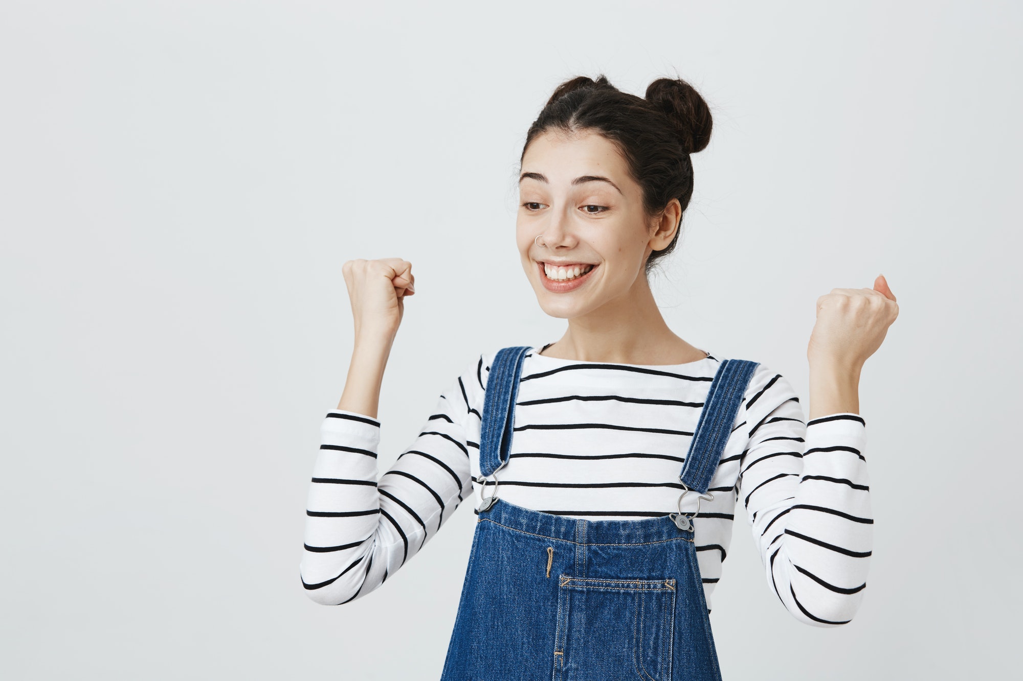 Excited brunette girl with hairbuns in striped top and denim clothes glad to achieve sucess