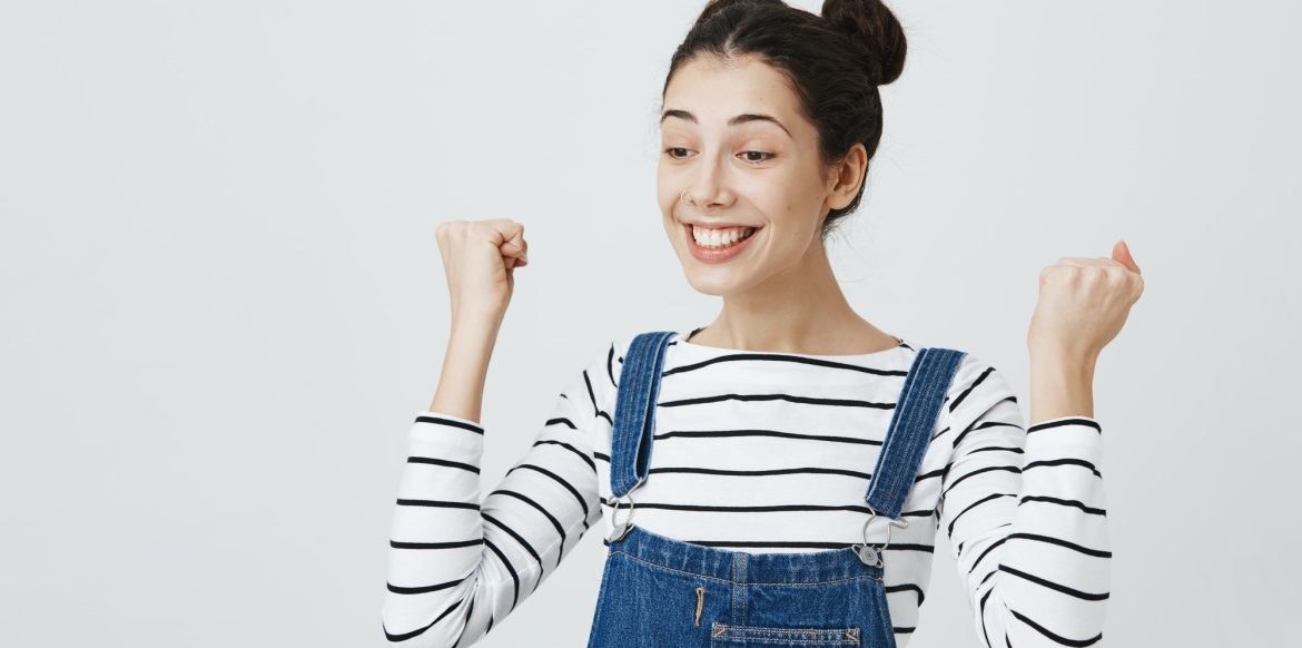 Excited brunette girl with hairbuns in striped top and denim clothes glad to achieve sucess